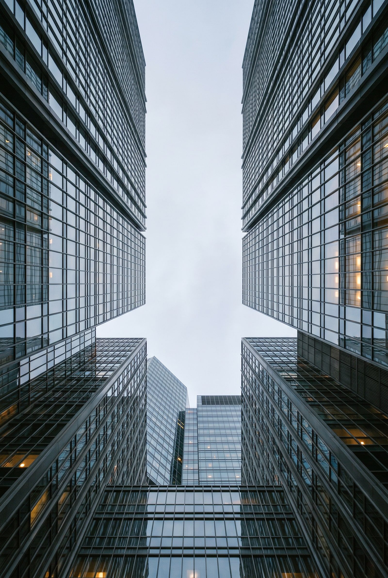 Looking straight up between glass office towers to a pale strip of sky.